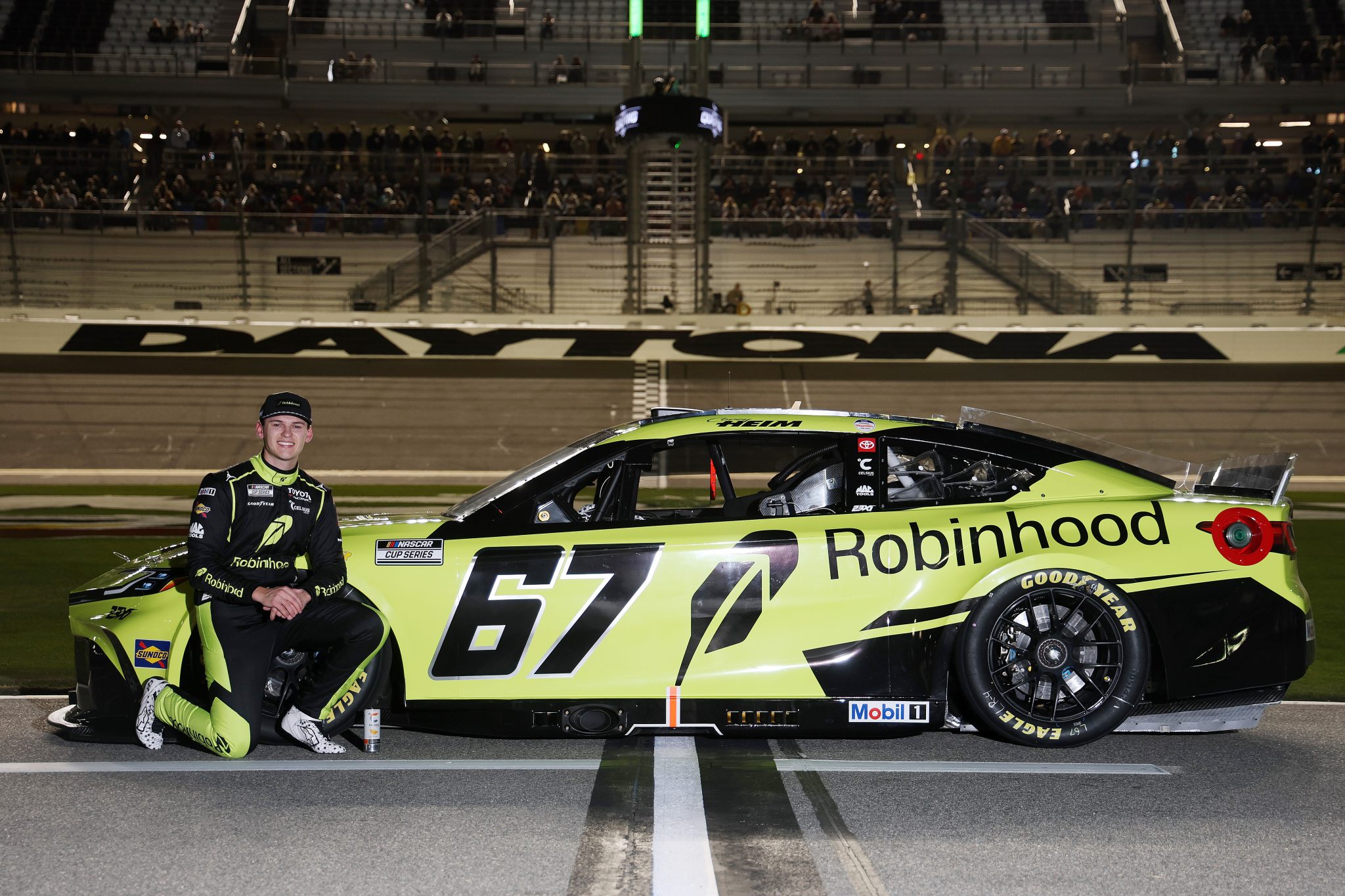 Corey Heim posing beside the number 67 Robinhood race car at Daytona